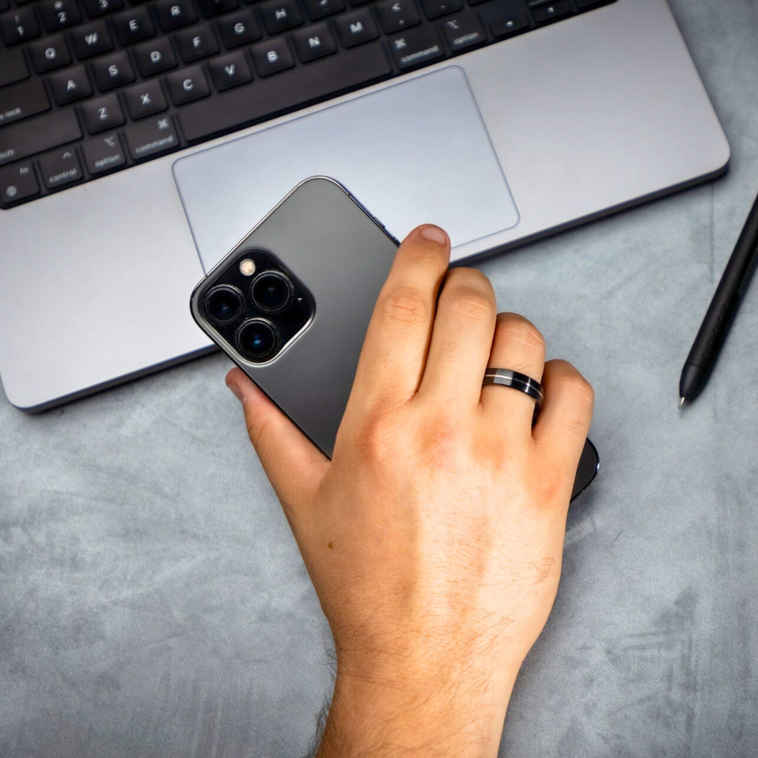 NFC Ring on a finger with an iphone and macbook in the background